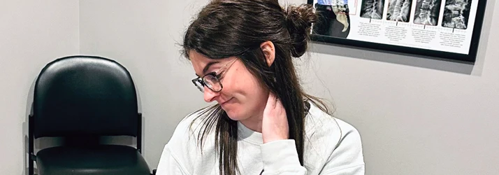A patient with dark brown hair holding her neck.