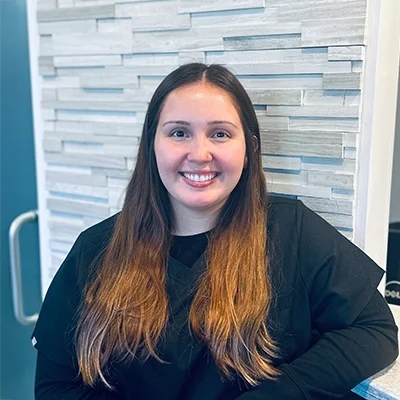 Front Desk Coordinator Hailie Smiling In Front Of Tile Wall
