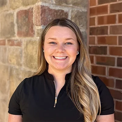Chiropractor Allie Wiseman Smiling In Front Of Bricks
